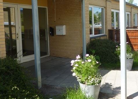 Lundens ingang ses udefra hvor der er blomsterkrukker på en sommerdag Billede af Lundens indgang